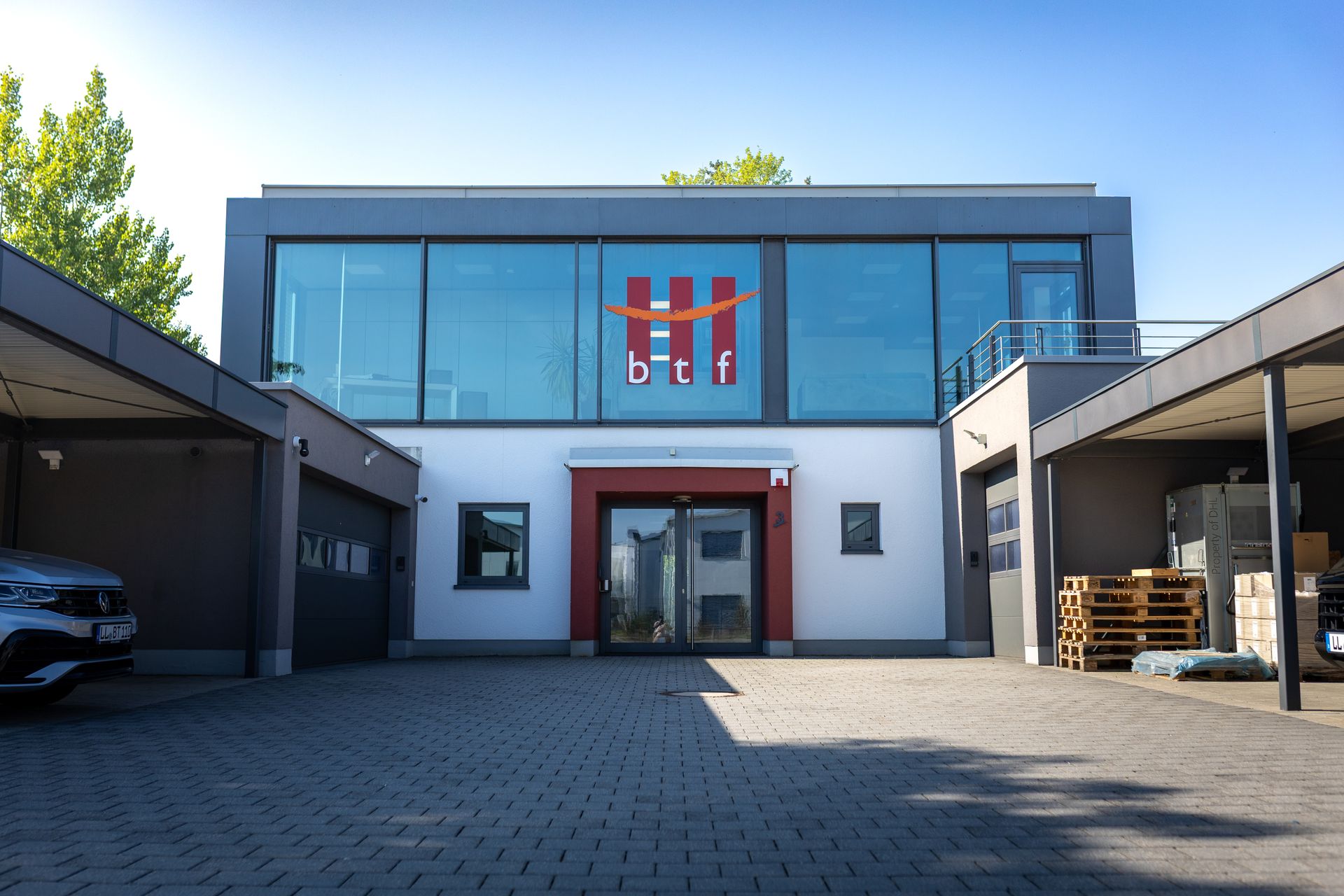 Modernes zweigeschossiges Bürogebäude mit großen Glasfenstern und rotem Logo mit den Buchstaben 'btf'
